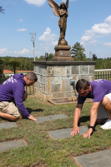 Dustin Owens and Andrew Perez weed around markers placed in honor of former residents who left the program and succumbed to their addictions. 