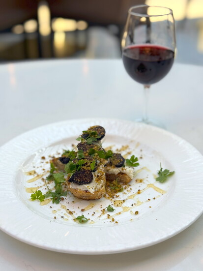Grilled bread layered with figs, pistachio and creamy ricotta, artfully plated and served with a glass of Pinot Noir Reserve at Versailles. 