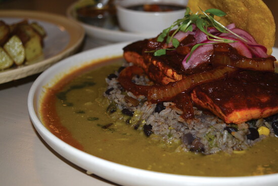 The Salmon al Pastor arrives bold and vibrant—topped with caramelized onions and pickled radish over black bean rice, all swimming in a golden pool of guajillo.
