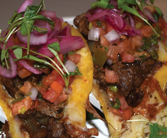 Grilled ranchera steak tacos at LUNA come stacked with juicy marinated beef, melted cheese, pico de gallo, and tangy pickled onions.