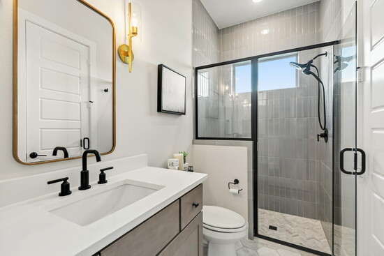 A modern secondary bath features a sleek vanity, chic tile shower, and stylish black fixtures. 