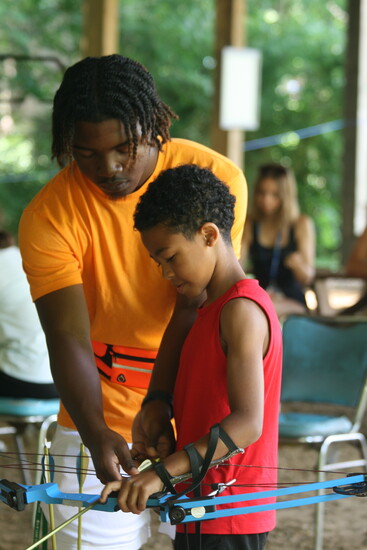 4-H Camp June 2024, Darreon helps Roman load his arrow for the first time. Roman Bost(age 9) and Camp Counselor, Darreon Barner) Photo Credit: Allyson Henschel.