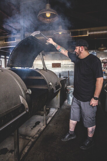 The Switch pitmaster lifts the heavy lid of the smoker as a cloud of fragrant smoke escapes