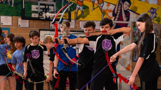 Focused young archers draw their bows in unison during a practice session, demonstrating skill and concentration