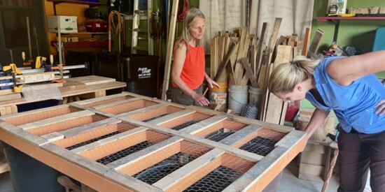 Shari Gullo (L) and Pam Self discuss the use of reclaimed wood covering the raw edges of the chicken wire encasing each piece of the installation.