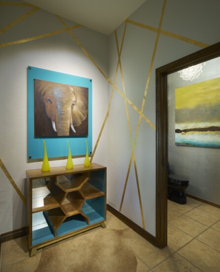 This elephant graphic was placed in an acrylic frame Pantone matched to the chest while abstract gold leaf stripes on the wall tie in with the bathroom’s metall