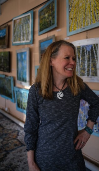 Deb smiling amongst her paintings in her shop at HWY 3 Plaza.