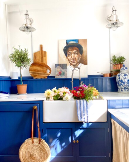 In the utility room, a painting by Miller depicting a friend gazes from above Aegean blue cabinets. 
