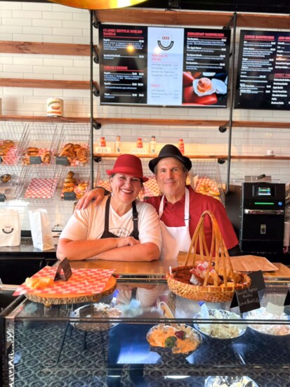 Julie Dragich and Steven Novotny, owners of The Bronx Bagel Buggy, stand behind the counter with their bagels and pasties.