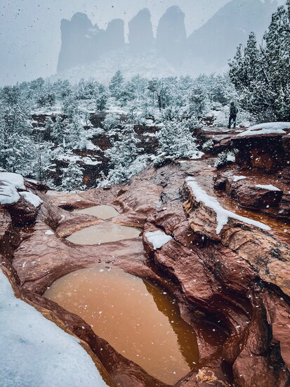 A hiker photographed near the Seven Sacred Pools during snowfall in Sedona, Arizona