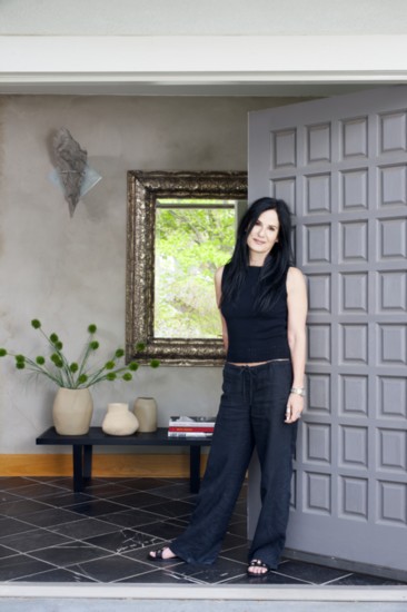 Designer Deborah Kalkstein at the entrance of her house, which combines antiques and modern style. Concrete wall in the back with antique silver mirror
