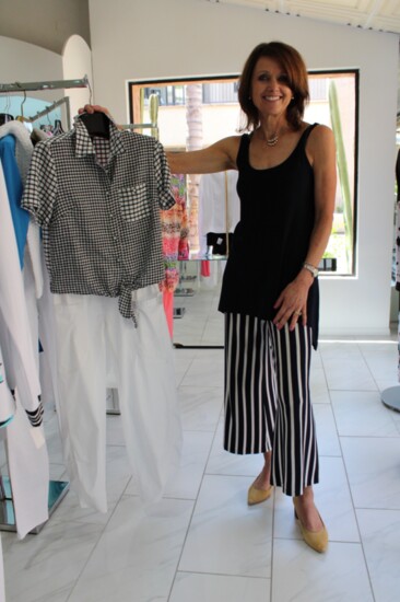 Kara Moeller, owner of La Contessa, holds a hanger with white cropped pants and a checkered top.La Contessa has been styling Tucson women for 36 years.