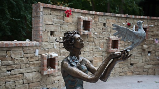 A unique statuette of a woman releasing a dove positioned in front of the memorial wall.