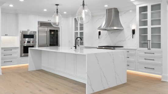 In the expansive kitchen, a full-wall porcelain backsplash is echoed on the waterfall-edged oversized island. LED baseboard lighting elevates and warms.
