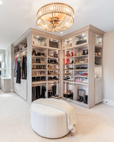 A walk-in closet with a vanity in a light-gray wood grain has ample storage for a stunning shoe collection. 