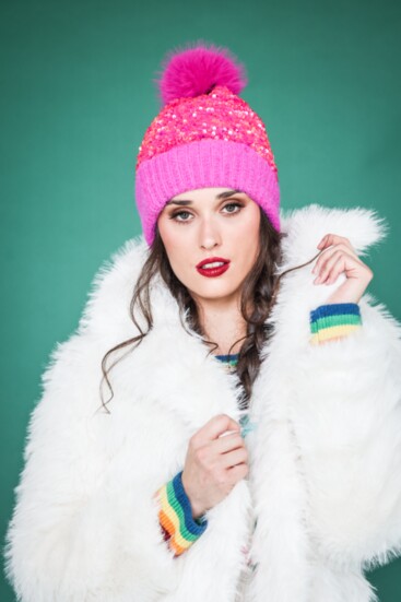 White faux fur thigh-length jacket from Molly Bracken combined with a sequin hot pink beanie. “Merry and Bright” sweater from Metric