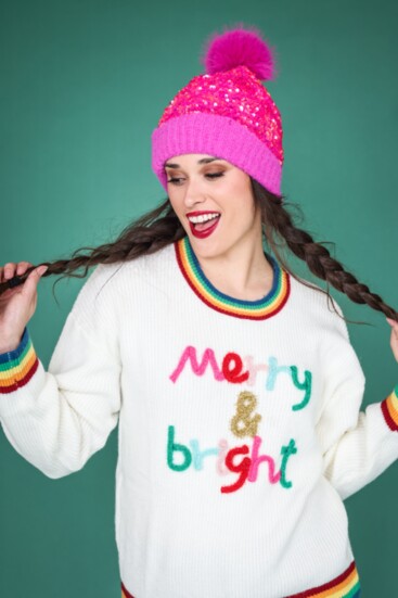 White faux fur thigh-length jacket from Molly Bracken combined with a sequin hot pink beanie. “Merry and Bright” sweater from Metric