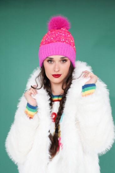 White faux fur thigh-length jacket from Molly Bracken combined with a sequin hot pink beanie. “Merry and Bright” sweater from Metric