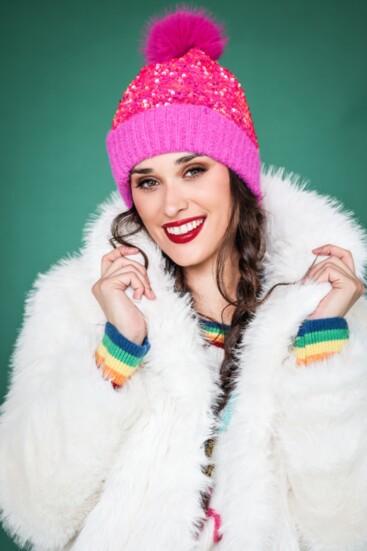 White faux fur thigh-length jacket from Molly Bracken combined with a sequin hot pink beanie. “Merry and Bright” sweater from Metric