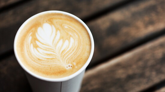 A latte in a to-go cup on a wooden table.