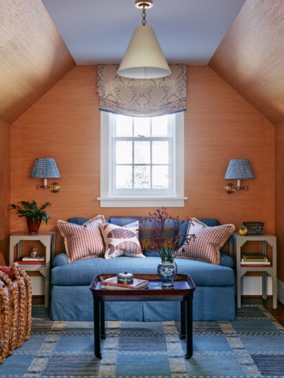 Warm beige grasscloth by Clarence House covers the walls of the den, where an antique tray table from Kenny Ball Antiques sits in front of the cozy blue sofa.  