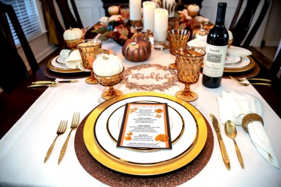 A table setting featuring metallic chargers, china, gold serving pieces, candles and Noritake glassware.