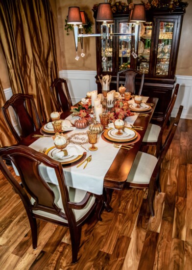 The completed table setting features metallic chargers, china, gold serving pieces, greenery, pumpkins, candles and Noritake glassware.