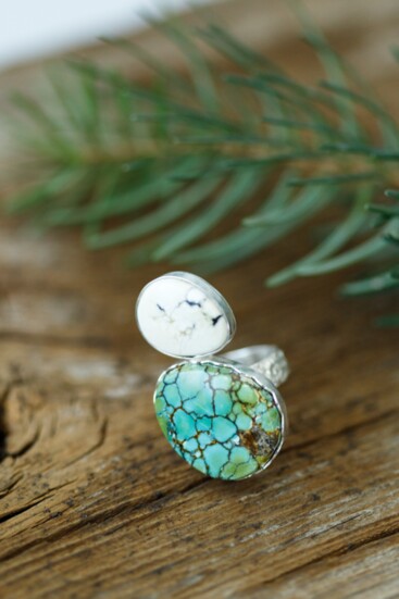 This ring features White Buffalo and Royston turquoise stones set on a bias to represent river rocks balancing on a band with a textured flower pattern. 