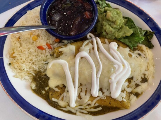 Enchiladas Verdes with two chicken enchiladas topped with green tomatillo sauce, Monterrey Jack cheese and sour cream with guacamole, rice and black beans is a 