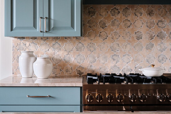 A natural stone backsplash introduces subtle texture and variation while complementing the space's soft blue cabinetry.