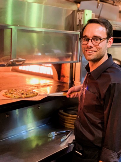 Harrison Sikes, Oliveto manager, pulls a hand-tossed pizza out of the woodstone oven.
