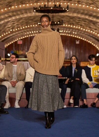 Seen on Tommy Hilfiger’s Fall/Winter 2024 Runway — oversized cable knit turtleneck paired with a pleated tweed skirt. Usa.tommy.com.