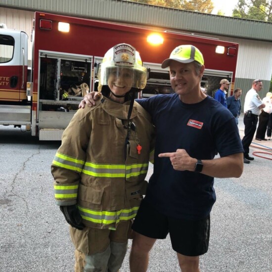 Mary Catherine Domaleski dons turnout gear before putting out a fire during the Fayette County Citizen's Fire Academy. Husband, Joe, offers moral support.