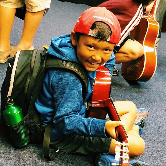 A young student beams with pride while learning guitar at The Art of Music Studio.