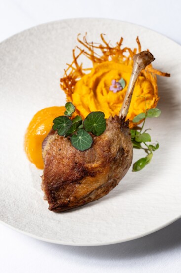 Duck confit with poached peach and yam puree in potato nest