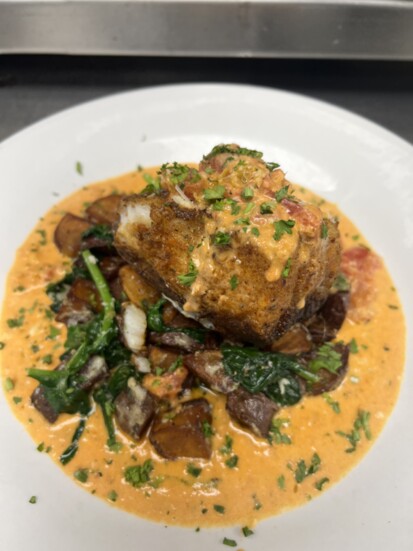 Blackened sea bass served with a broken tomato cream sauce, crispy potatoes and sautéed spinach