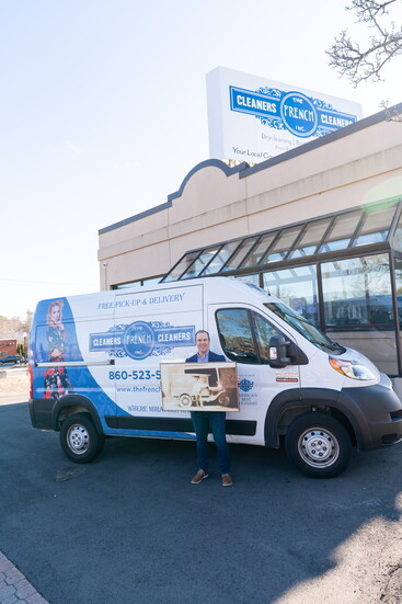 Mark Hatch holds a historic photo of The French Cleaners in front of one of the company's vans. 