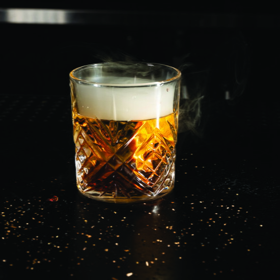 Smoke wafts atop a whiskey cocktail.