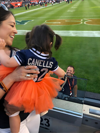 Monica lifts baby Gia to greet dad on the sidelines. (Photo provided)