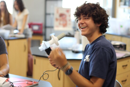 A student holds a device that measures lung capacity and volume.  In this lab, students tested their lung power under different scenarios.