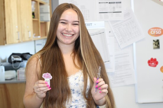 Student holds prizes, including a pen shaped like a hypodermic needle, that she won in class game.