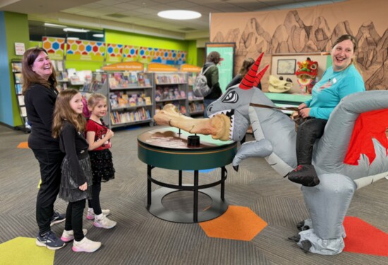 Teen Librarian Sonya Hill on her inflatable dragon laughs with patrons at the giant bone exhibit at the Ela Area Public Library. Photo: Jennifer Nickels.