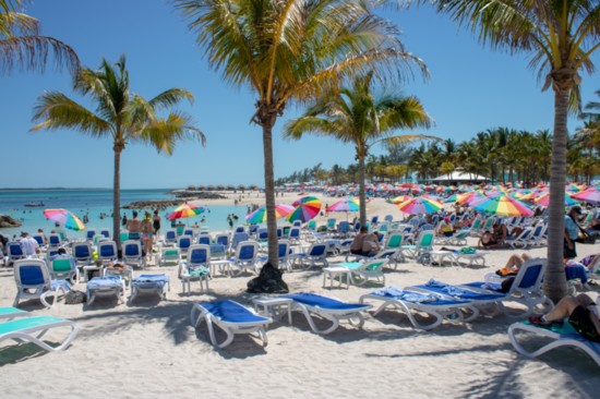 A sandy beach at CocoCay with colorful rainbow umbrellas on a sunny day.