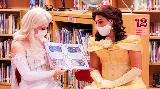Elsa and Belle read a book to children at an elementary school library.
