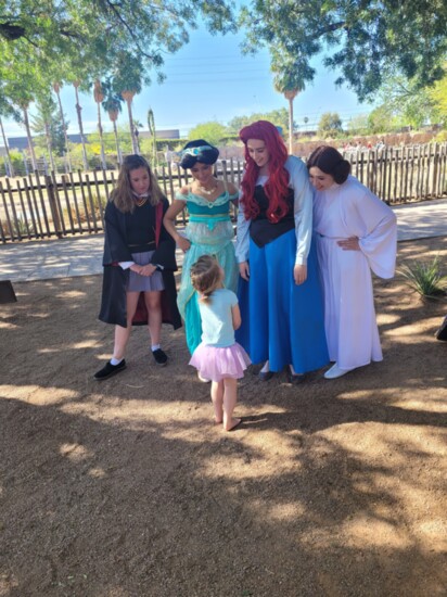 A little girl looks excitedly up to Hermione, Jasmine, Ariel, and Princess Leia. 