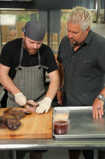 Host Guy Fieri observing Chef and Owner Andrew Samia at Work in the Kitchen at Dignowity Meats in San Antonio, Texas, as seen on Diners, Drive-ins and Dives