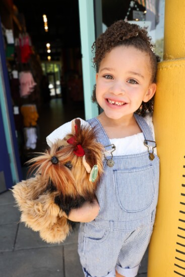 Moira models a Mayoral white eyelet top with Dotty Dungarees striped overalls. The Yorkie comes from Bearington Bears.