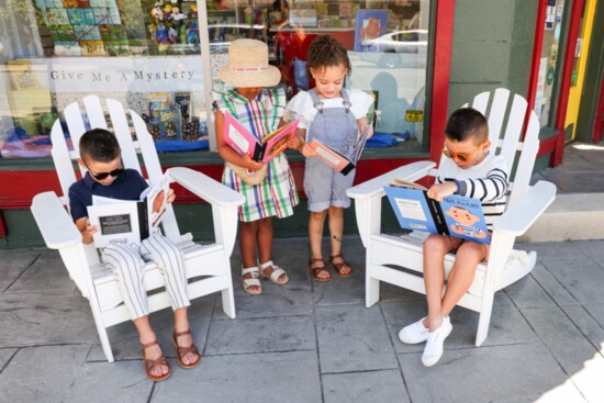 On the left, Noah wears a Mayoral navy knit polo with striped pants, and the kids' books come from the Little People, Big Dreams series.