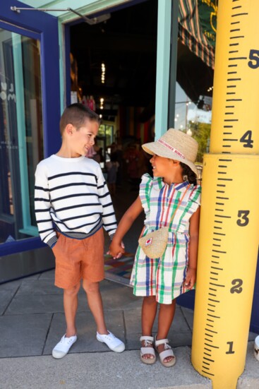 Liam wears a Mayoral sweater with Miles the Label linen shorts, and Nora is decked out in a Bobo Choses plaid dress, straw hat and purse.