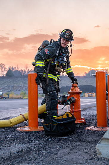 Firefighter T. Dilley stands at a fire hydrant during a live burn scenario at sunset